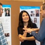 An honoree shares in conversation with two reception attendees, standing by the poster displays.