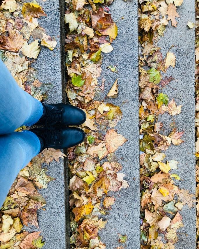 Simar's boots as she stands on rain-slicked stone steps covered in fallen leaves.