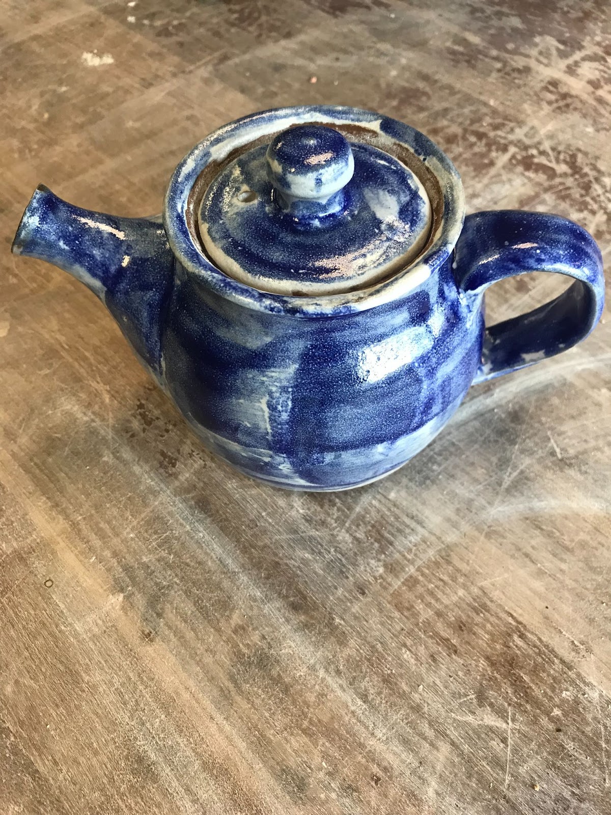 A teapot glazed so that it looks like it has been watercolor painted with deep blue color.