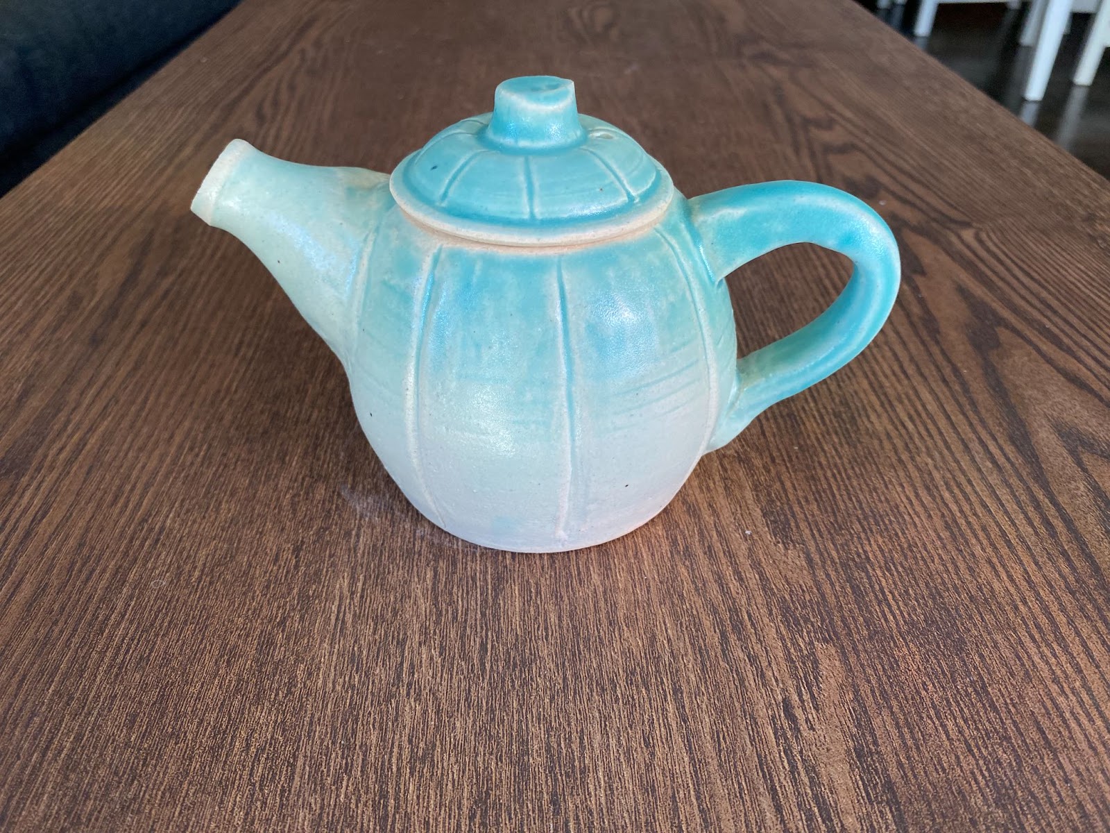 A light, bright blue teapot scored with lines around its body, giving the impression of a pumpkin shape.