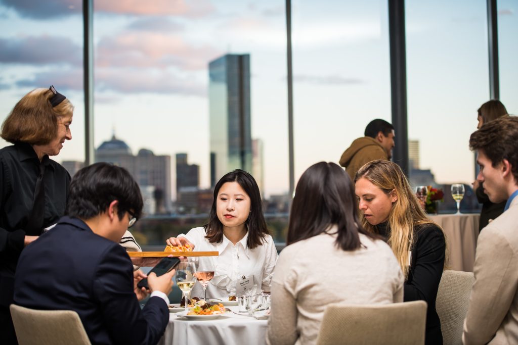 A Presidential Fellow reaches for a passed appetizer from a tray while sitting with other fellows at a table.